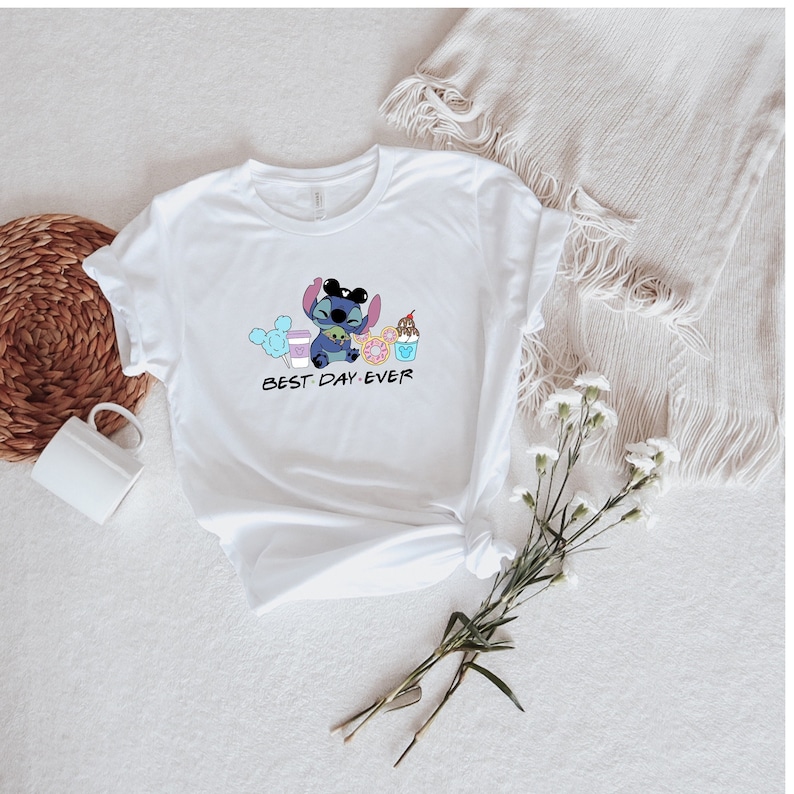 May include: White t-shirt with a blue Stitch character wearing sunglasses and holding a green alien. Stitch is surrounded by cartoon images of food and drinks. The text "BEST DAY EVER" is printed below Stitch.