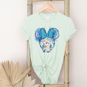 May include: A light green t-shirt with a blue and white illustration of a Disney princess with a blue bow and a castle in the background.