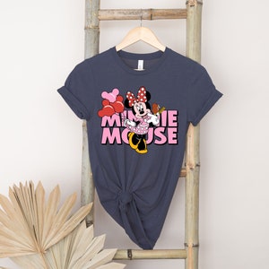 May include: A dark blue t-shirt with a pink and red Minnie Mouse graphic. The graphic features Minnie Mouse holding a red balloon and a pink and white polka dot dress. The text "Minnie Mouse" is written in pink letters.
