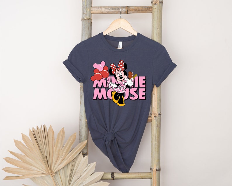 May include: A dark blue t-shirt with a pink and red Minnie Mouse graphic. The graphic features Minnie Mouse holding a red balloon and a pink and white polka dot dress. The text "Minnie Mouse" is written in pink letters.