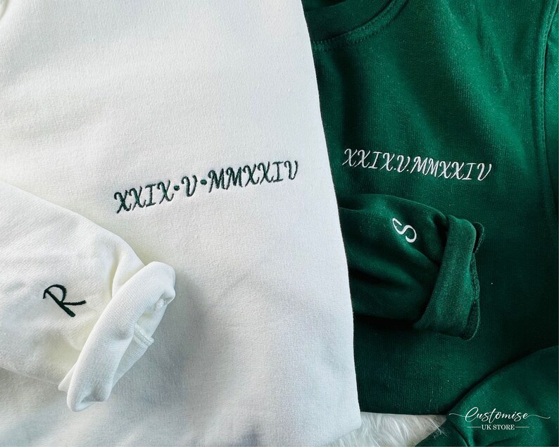 Peut inclure: Deux sweats blancs avec des broderies vertes. Un sweat-shirt a le texte "XXIX - V - MMXXI" et la lettre "R" brod&eacute;e sur la manche. L'autre sweat-shirt a le texte "XXIX.V.MMXXI" et la lettre "S" brod&eacute;e sur la manche.