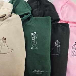 Pode incluir: Quatro sweatshirts com capuz em cores diferentes, cada uma com um design bordado diferente de duas pessoas se abra&ccedil;ando. Os designs s&atilde;o em branco e as sweatshirts s&atilde;o bege, verde, preto e rosa.
