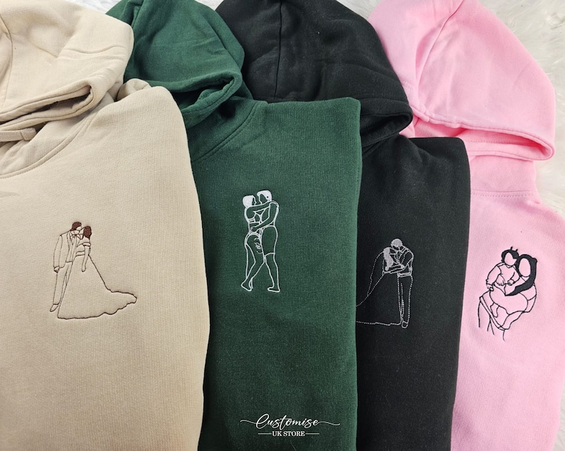 Pode incluir: Quatro sweatshirts com capuz em cores diferentes, cada uma com um design bordado diferente de duas pessoas se abra&ccedil;ando. Os designs s&atilde;o em branco e as sweatshirts s&atilde;o bege, verde, preto e rosa.