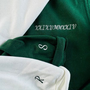 Peut inclure: Deux chemises &agrave; manches longues, une blanche et une verte. La chemise verte a le texte "XXIX.V.MMXXVI" brod&eacute; sur le devant. La chemise blanche a un petit "R" brod&eacute; sur le devant.