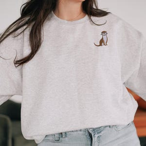 Peut inclure: Un sweat-shirt gris avec une petite loutre brod&eacute;e sur la poitrine gauche.