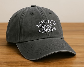 May include: A dark grey baseball cap featuring the white text "LIMITED EDITION 1963". The cap has a curved peak and a button on top. The hat is made of a soft, worn material.