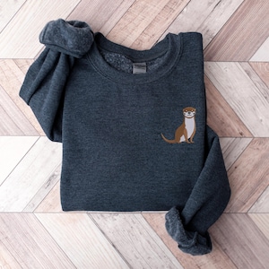 Peut inclure: Un sweat-shirt gris fonc&eacute; avec un graphique d'une loutre brune et blanche sur la poitrine gauche.