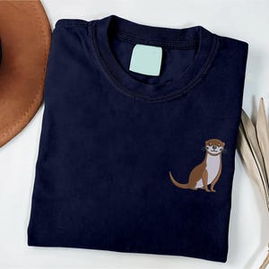 Peut inclure: Un t-shirt bleu marine avec une loutre brune brod&eacute;e sur le c&ocirc;t&eacute; gauche de la poitrine.