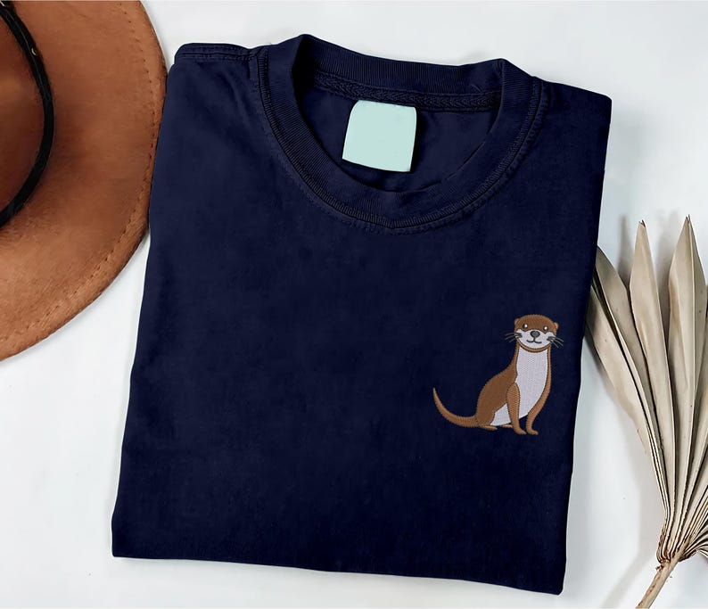 Peut inclure: Un t-shirt bleu marine avec une loutre brune brod&eacute;e sur le c&ocirc;t&eacute; gauche de la poitrine.