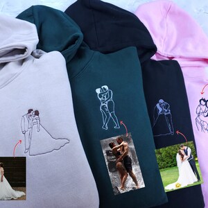 Pode incluir: Quatro sweatshirts com capuz em diferentes cores, cada uma com um design bordado personalizado. Os designs incluem um casal a beijar-se, um casal a dar-se as m&atilde;os, um casal a abra&ccedil;ar-se e um casal a segurar um beb&eacute;. As sweatshirts est&atilde;o dispon&iacute;veis em cinzento, verde, preto e rosa.
