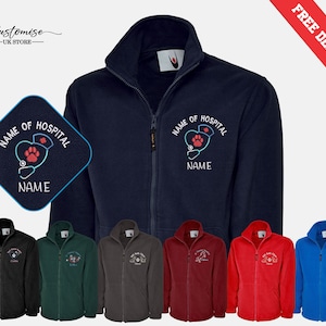 Può includere: Giacca in pile blu navy con chiusura a zip e logo ricamato bianco che dice "Nome dell'ospedale" con uno stetoscopio e un'impronta di zampa. La giacca è disponibile in una varietà di colori, tra cui nero, verde, grigio, bordeaux, rosso e blu.