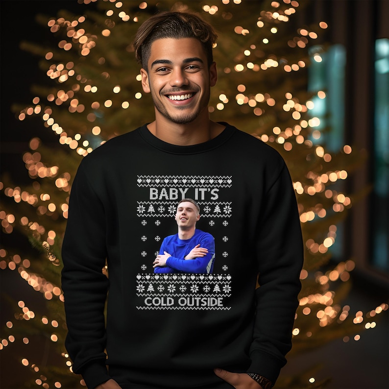 May include: A black Christmas sweater with a white snowflake pattern and the text "Baby It's Cold Outside". A photo of a person is in the center of the sweater.
