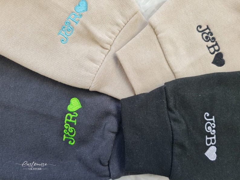 Pode incluir: Quatro sweatshirts de cores diferentes com o texto "J&R" ou "J&B" bordado nelas. Cada sweatshirt tem um pequeno cora&ccedil;&atilde;o bordado ao lado do texto. As sweatshirts s&atilde;o bege, preto, cinza e cinza escuro.