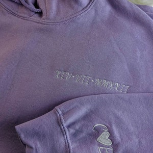 Peut inclure: Un sweat &agrave; capuche violet avec le texte "XIV - VII - MMXXII" brod&eacute; sur le devant et les lettres "C&B" avec un c&oelig;ur brod&eacute; sur la manche gauche.