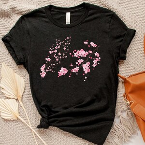 Puede incluir: Una camiseta negra con un dise&ntilde;o de flores de cerezo rosas. La camiseta est&aacute; hecha de un material suave y c&oacute;modo y tiene un corte holgado.