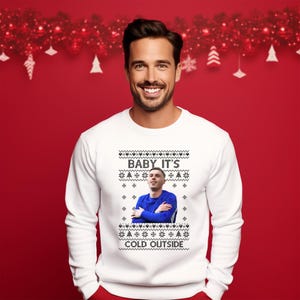 May include: White Christmas sweater with a black and white snowflake pattern. The sweater features a photo of a person with the text "Baby It's Cold Outside".