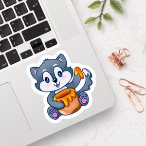 Könnte beinhalten: Ein grauer Cartoon-Wolf mit rosa Pfoten und einem breiten Lächeln hält einen Honigtopf. Der Wolf trägt einen gelben und orangen Honigtopf mit einem gelben Honigtropfen auf seiner Pfote.