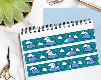 May include: A washi tape with a repeating pattern of blue mountains, white clouds, and green and purple hearts on a teal background.