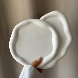 May include: Two white ceramic plates with an organic, wavy edge. The plates are stacked on top of each other.