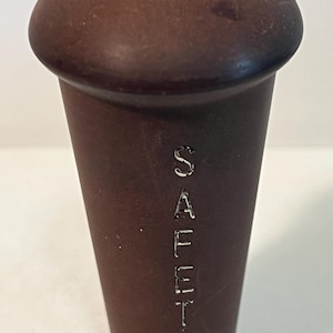 May include: A brown, cylindrical object with a rounded top. The word "SAFETY" is vertically etched into the side. The object appears to be made of a solid, possibly wooden, material. The design is simple and functional.