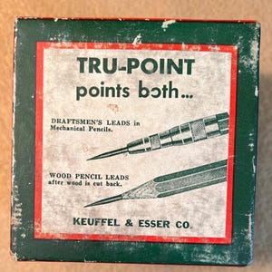 May include: Vintage box with the text "TRU-POINT points both..." in white lettering on a beige background, framed by a red border. The box features illustrations of mechanical pencil leads and wood pencil leads. The bottom of the box reads "KEUFFEL & ESSER CO."