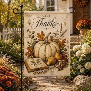 Puede incluir: Una bandera de jardín rectangular con el texto "GIVE Thanks" en caligrafía negra. El diseño incluye una calabaza grande central, dos peras, un libro abierto con ilustraciones botánicas, hojas de otoño, espigas de trigo y setas.