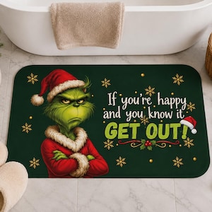 Könnte beinhalten: Eine rechteckige dunkelgrüne Badematte mit einer grünen Figur, die eine rote Weihnachtsmütze und einen Mantel mit weißem Pelzbesatz trägt. Der Text lautet, If you're happy and you know it GET OUT! Das Design enthält goldene Schneeflocken.