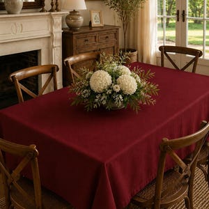 Puede incluir: Un mantel rectangular de color rojo intenso cubriendo una mesa de comedor, con una superficie de tela lisa y de color sólido que se extiende hasta los bordes de la mesa, proporcionando un aspecto limpio y uniforme al mueble.