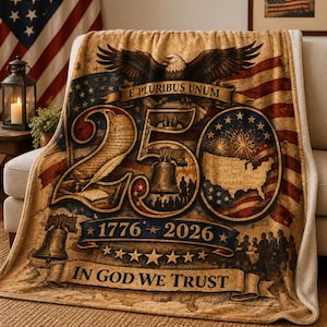 May include: A tan and cream-coloured blanket with an American flag design. The blanket features an eagle, the text "E Pluribus Unum", the Liberty Bell, and the text "250", "1776-2026", and "In God We Trust".