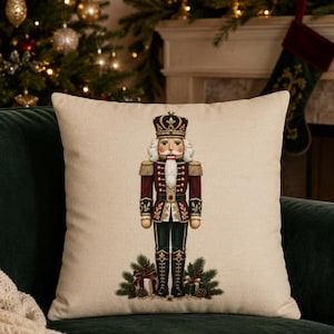 May include: A square beige pillow cover featuring a central illustration of a nutcracker soldier in a red, green, and gold uniform with a crown. The text PILLOW COVER ONLY NO INSERT is printed in a circle in the upper right corner of the image.