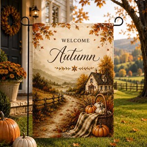 Könnte beinhalten: Eine rechteckige Gartenflagge mit dem Text "WELCOME Autumn" in schwarzer Schreib- und Serifenschrift. Die Abbildung zeigt eine ländliche Landschaft mit einem Steinhäuschen, einem Feldweg, einem Korb voller Kürbisse und einer karierten Decke.