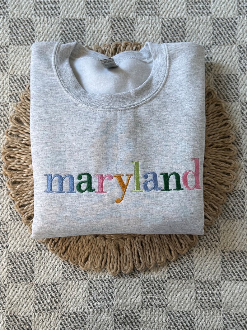 May include: Gray sweatshirt with the word "maryland" embroidered in colorful letters.
