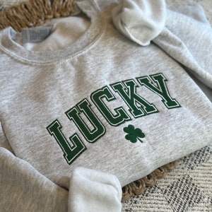 May include: A gray sweatshirt with the word "LUCKY" embroidered in green with a green four-leaf clover.