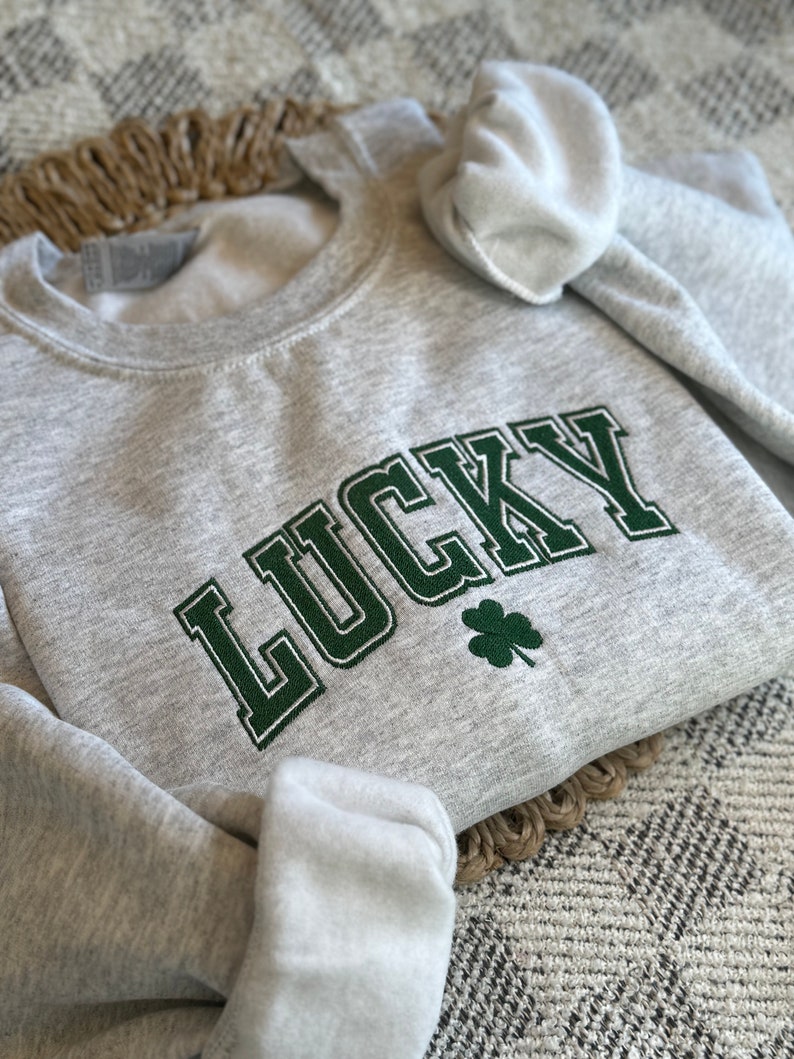 May include: A gray sweatshirt with the word "LUCKY" embroidered in green with a green four-leaf clover.