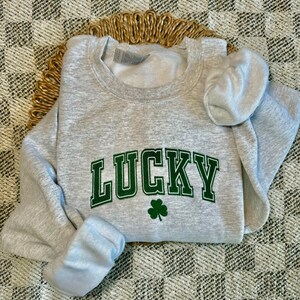 May include: A gray sweatshirt with the word "LUCKY" in green letters with a green four-leaf clover underneath.
