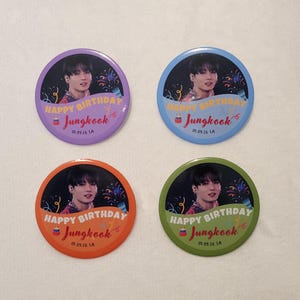 May include: Four circular pin-back buttons featuring a portrait of a person, confetti, and the text "HAPPY BIRTHDAY Jungkook" with a small cake icon and "01.09.16 LA". The buttons have purple, blue, orange, and green borders respectively.