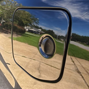 May include: A black car with a gas cap door. The door is open and the gas cap is visible. The car is parked on a paved surface.