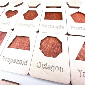 May include: Wooden learning toy with different shapes, including a heart, hexagon, rectangle, pentagon, trapezoid, octagon, and triangle. Each shape has a corresponding label.