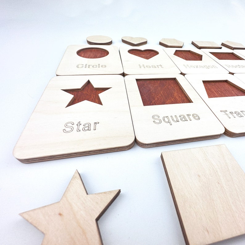 May include: Wooden puzzle pieces with cutouts of different shapes, including a circle, heart, hexagon, star, square, and triangle. Each piece has the name of the shape written below the cutout.