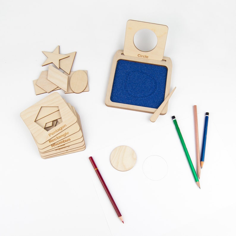 May include: Wooden geometric shapes learning toy with a blue felt board and a wooden stylus. The shapes include a circle, star, pentagon, rectangle, rhombus, and a few other shapes. The shapes are labeled with their names. There are also four colored pencils on the white surface.