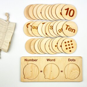 May include: Wooden learning set with 10 round pieces featuring numbers, words, and dots. The set includes a wooden board with three slots labeled "Number", "Word", and "Dots".