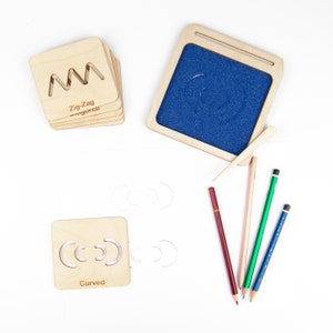 May include: A set of wooden tracing boards for kids to practice drawing different lines. The boards include a zig-zag, curved, and straight line. The set also includes a small wooden tray with blue sand and a wooden stylus.