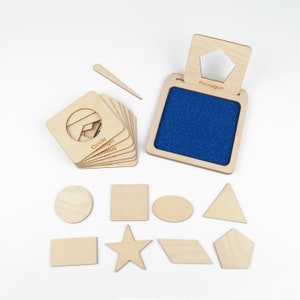 May include: Wooden shape stamps with a blue felt pad for stamping. The shapes include a circle, triangle, square, star, oval, rhombus, pentagon, and rectangle. The stamps are labeled with the name of each shape.