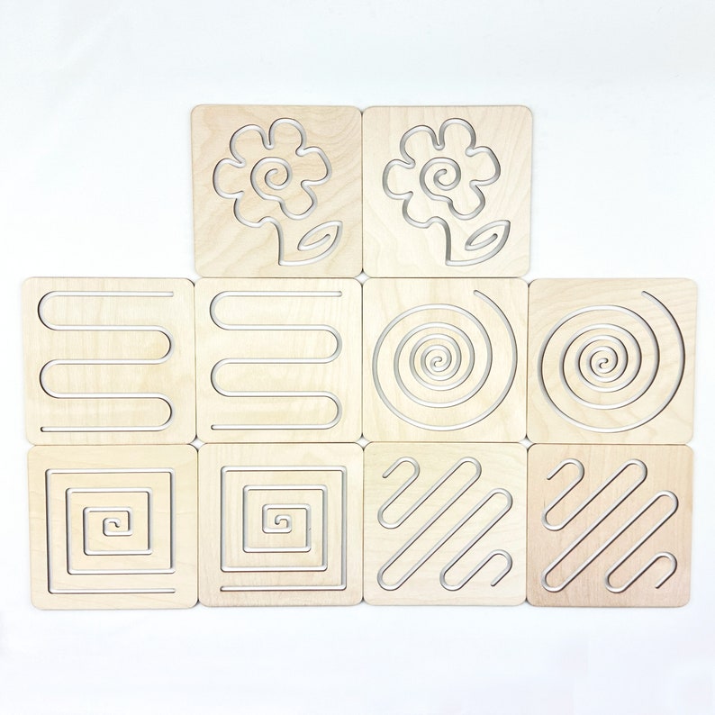 May include: Set of ten wooden tracing boards with various patterns, including spirals, squares, and flowers. The boards are light brown and the patterns are silver.