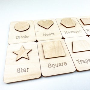 May include: Wooden learning cards with cutouts of different shapes, including a circle, heart, hexagon, square, star, and trapezoid. Each card has the name of the shape printed below the cutout.