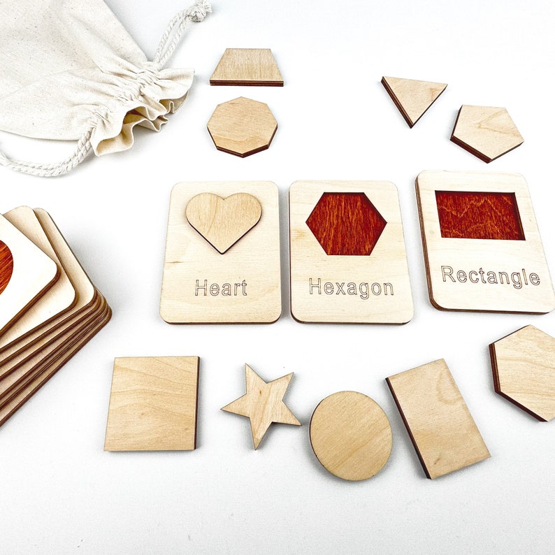 May include: Wooden shape puzzle with a variety of shapes including a heart, hexagon, rectangle, star, circle, and square. The shapes are labeled with their names. The puzzle is made of natural wood and has a light brown color.