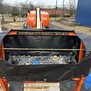 May include: A black cover for an aerial work platform control panel. The cover is made of a durable material and has a zipper closure. The cover is designed to protect the control panel from the elements and debris.