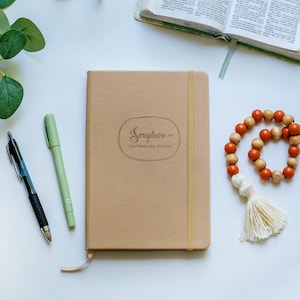 May include: A brown leather-bound journal with a gold elastic closure. The journal has the words "Scripture Mapping Mini Journal" embossed on the front cover.