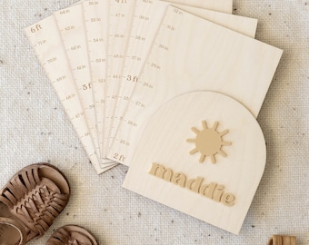 May include: A wooden growth chart with a sun and the name "maddie" on it. The chart has a ruler on the side that measures in inches and feet. There are also several smaller rulers that measure in inches. The chart is sitting on a beige rug.