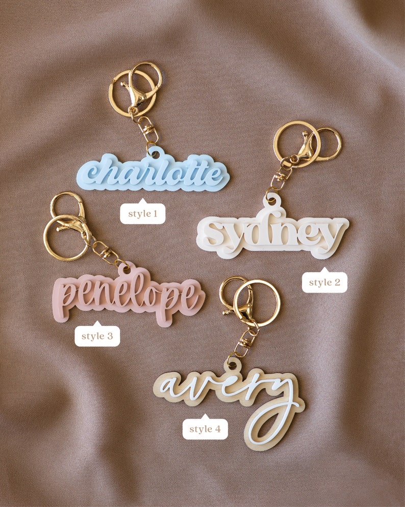 May include: Four personalized keychains with different styles. The keychains feature the names "Charlotte", "Sydney", "Penelope", and "Avery". Each keychain has a gold metal ring and a different colored acrylic name tag.